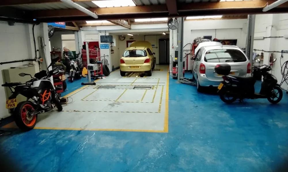 Inside the Herons Autos workshop — the MOT bay, a lift with a car on it, and motorcycles in for work